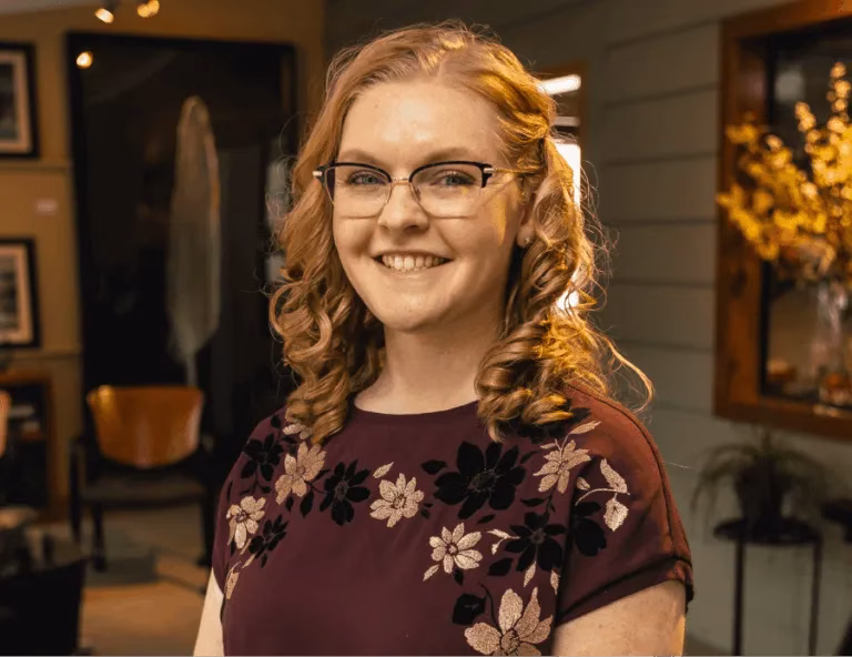 Smiling woman with glasses and curled hair wearing a floral top indoors